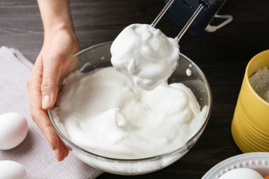 Siyah ahşap masada yumurta beyazlarını el çırpıcı ile çırpan kadın, yakın plan.