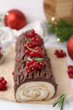 Lezzetli Noel kütüğü (geleneksel Noel pastası) kırmızı frenk üzümü ve dekorlu beyaz masa, yakın plan