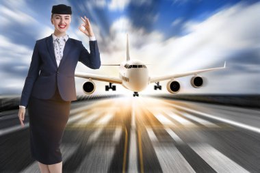 Üniformalı hostes podyumda gülümsüyor. Arkasından uçak iniyor.