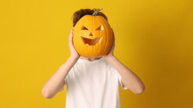 Cadılar Bayramı kutlaması. Çocuk, turuncu arka planda oyulmuş ürkütücü yüzlü balkabağı tutuyor.