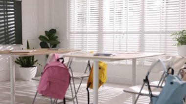 Sınıfta yeşil karatahta, masalar ve sırt çantalı sandalyeler. Kamera sola hareket ediyor