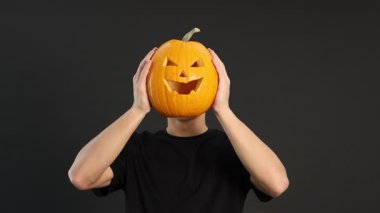 Cadılar Bayramı kutlaması. Siyah arka planda oyulmuş ürkütücü yüzü olan bir adam balkabağı tutuyor.