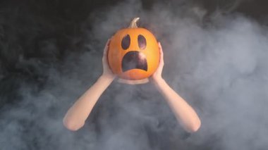 Cadılar Bayramı kutlaması. Siyah arka planda çizilmiş ürkütücü yüzlü balkabağı tutan çocuk dumanlı