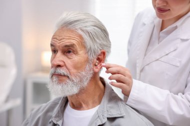 Doktor hastanede yaşlı adamın kulağına işitme cihazı takıyor.
