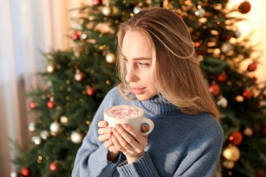 Evdeki Noel ağacının yanında kakao içen kadın.