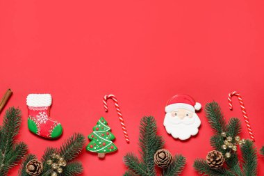 Köknar ağacı dalları, Noel dekoru, kurabiyeler ve kırmızı arka planda şeker kamışları olan düz bir kompozisyon. Metin için boşluk