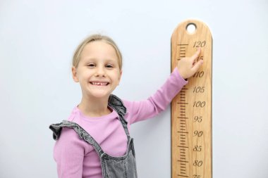 Açık gri duvarın yanında boyunu grafikle ölçen küçük bir kız.