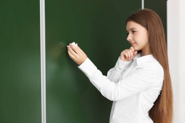 Okula dönelim. İçerideki yeşil karatahtaya tebeşirle yazı yazan öğrenci