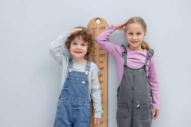 Küçük bir çocuk ve kız açık gri duvarın yanında boylarını grafikle ölçüyorlar.