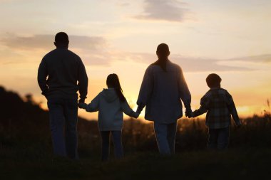 Aile gün batımında, arka planda el ele tutuşuyor.