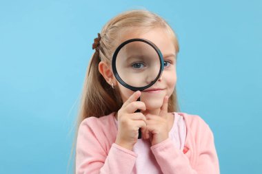Açık mavi arka planda büyüteç takan küçük bir kız.