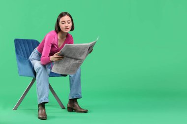 Güzel bir kadın gazete okuyor ve yeşil arka planda sandalyeye oturuyor. Metin için boşluk