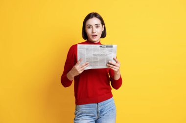 Sarı arka planda gazetesi olan sürpriz bir kadın.