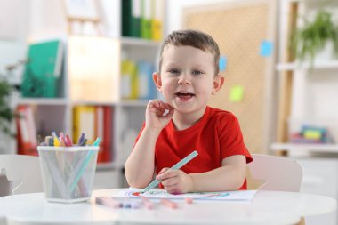 Beyaz masa içinde keçeli kalemle çizim yapan mutlu küçük çocuk.