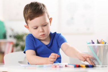 Beyaz masaya keçeli kalemle çizen sevimli küçük çocuk.