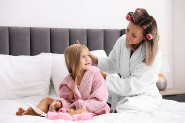 Saç bigudileri olan anne evde yatağında kızının saç modelini yapıyor.