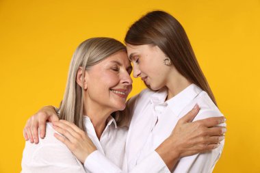 Anne ve kızı turuncu arka planda sarılıyorlar.