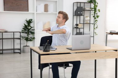 Genç işadamı kollarını uzatıp, masada oturuyor.