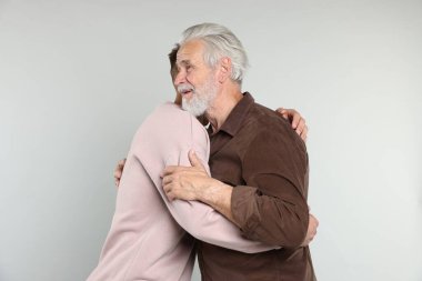 Baba ve oğul açık gri arka planda sarılıyorlar.