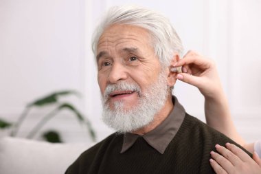 Bakıcı, kıdemli adamın evde işitme cihazı takmasına yardım ediyor.