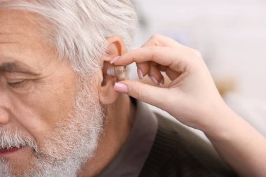 Bakıcı, kıdemli adamın evde işitme cihazı takmasına yardım ediyor.