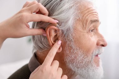 Bakıcı, kıdemli adamın evde işitme cihazı takmasına yardım ediyor.