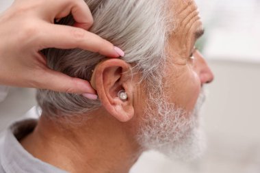 Doktor hastanede yaşlı adamın kulağına işitme cihazı takıyor.