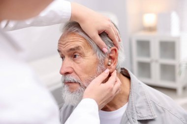 Doktor hastanede yaşlı adamın kulağına işitme cihazı takıyor.