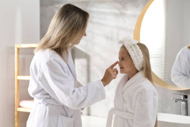 Anne banyoda kızının yüzüne krem sürüyor.