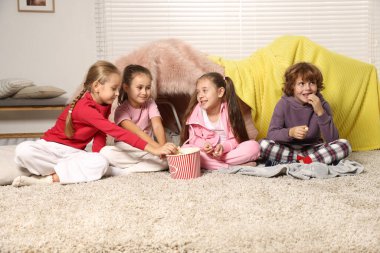 Pijamalı şirin çocuklar evde yerde patlamış mısır yiyor.