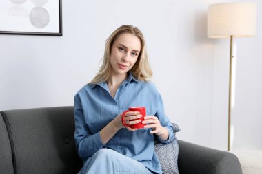 Evdeki kanepede bir fincan kakao içen kadın.