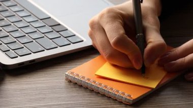 Ahşap masadaki yapışkan nota yeni şifre yazan kadın, yakın plan.