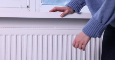 Kadın ellerini radyatörün yanında ısıtıyor, yakın plan.