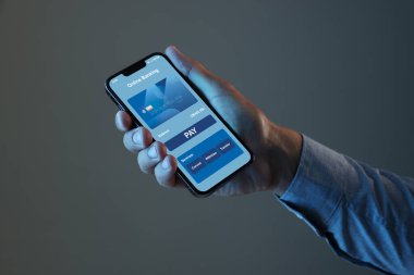 Çevrimiçi ödeme. Gri arkaplanı açık uygulamalı cep telefonu tutan adam, yakın plan.