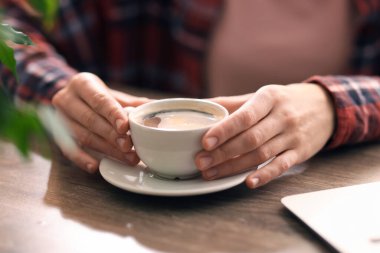Kahve molası. Ahşap masada bir bardak aromalı içki içen kadın, yakın plan.