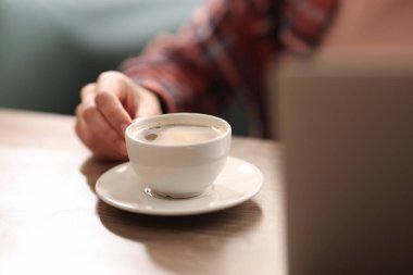 Kahve molası. Ahşap masada bir bardak aromalı içki içen kadın, yakın plan.