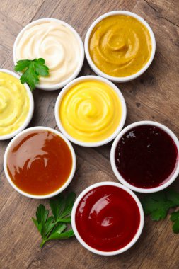 Tabaklardaki farklı lezzetli soslar ve ahşap masadaki maydanozlar.