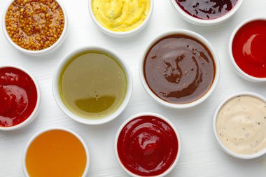 Tabaklardaki farklı soslar beyaz ahşap masada, düz yerde.