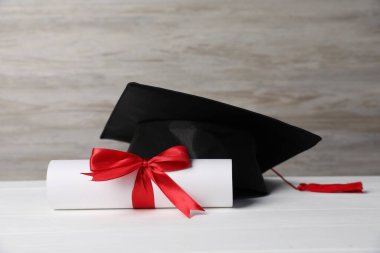 Mezuniyet şapkası ve diploması beyaz tahta masada.