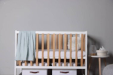 Beşik, depolama kutuları ve açık gri duvarın yanındaki masa bulanık görünüyor. Şık bir bebek odası.