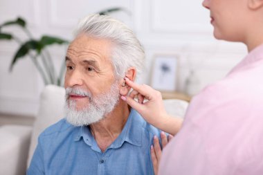 Bakıcı, kıdemli adamın evde işitme cihazı takmasına yardım ediyor.