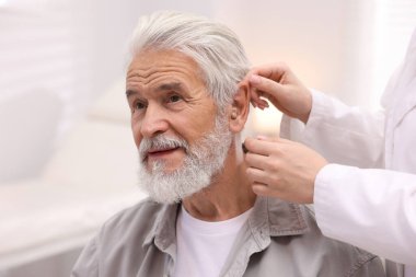 Doktor hastanede yaşlı adamın kulağına işitme cihazı takıyor.