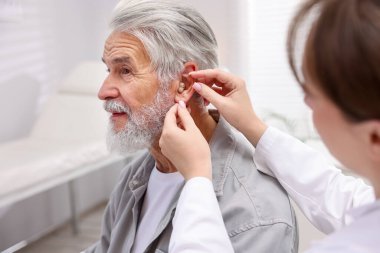 Doktor hastanede yaşlı adamın kulağına işitme cihazı takıyor.