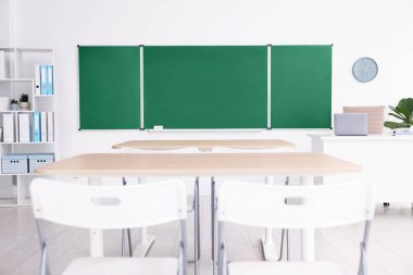 Sınıfta yeşil karatahta, masalar ve sandalyeler var. Tasarım için model