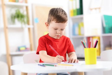 Beyaz masada renkli kalemler çizen sevimli küçük bir çocuk.