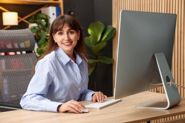 Ofisteki bilgisayarda çalışan genç bir kadın.