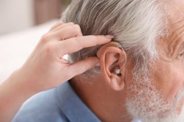 Bakıcı, kıdemli adamın evde işitme cihazı takmasına yardım ediyor.