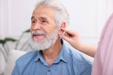 Bakıcı, kıdemli adamın evde işitme cihazı takmasına yardım ediyor.