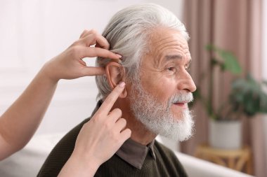 Bakıcı, kıdemli adamın evde işitme cihazı takmasına yardım ediyor.