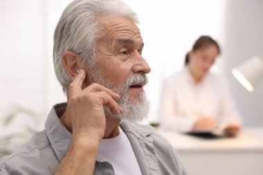 İşitme cihazı olan kıdemli bir adam ve hastanede çalışan bir doktor, seçici odaklı.